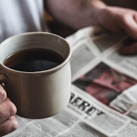 a man holding a cup of coffee while reading a newspaper